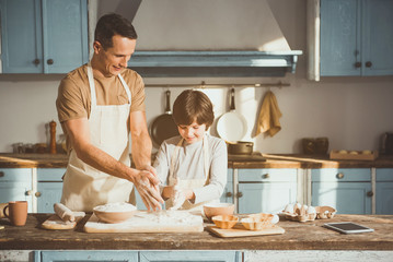 Father and son cooking with joy in kitchen. They touching flour with hands. Copy space in right side