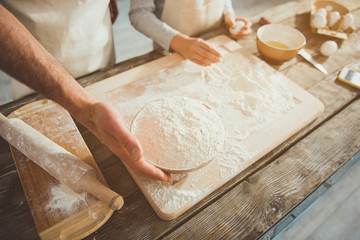 Close up of father and son cooking together. Focus on adult arms holding bowl with flour