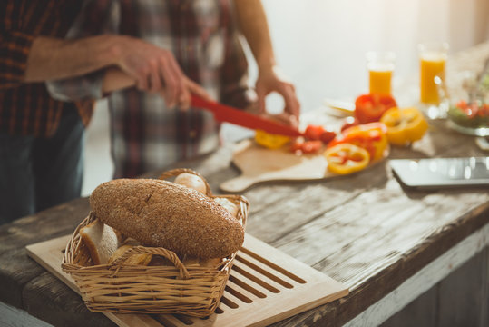 Focus on tasty bread on wooden table. Man and boy chopping ingredients for salad on background. Close up
