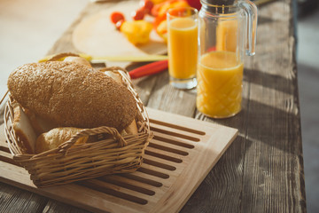 Close up of wooden desk with tasty bread, juice and vegetables on it. Focus on bakery