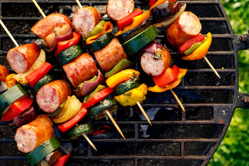 Grilled skewers of meat, sausages and various vegetables on a grill plate, outdoors, top view....