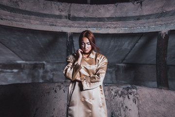 Abstract photo of a beautiful young woman in a beige silk coat against a background of concrete walls of an underground city station.