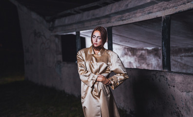 Naklejka premium Abstract photo of a beautiful young woman in a beige silk coat against a background of concrete walls of an underground city station.