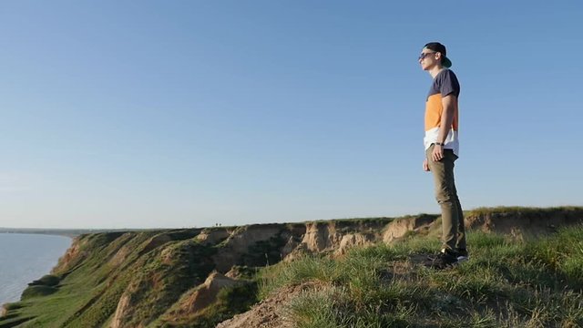 Profile of a brisk man in a baseball cap, sunglasses and a T-shirt standing on the Black Sea coast and enjoying the seascape in summer in slow motion