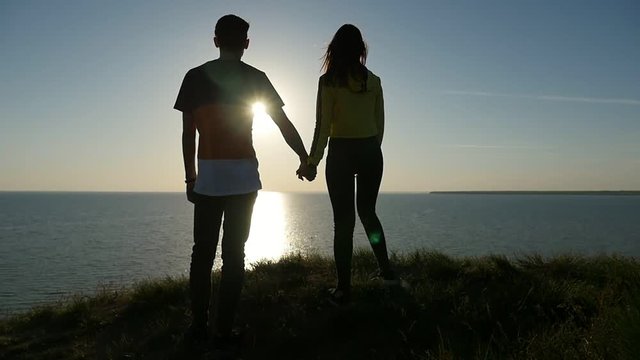 Back view with a zoom in of a romantic man with his happy girlfriend at a wonderful sunset with a sparklin sun path at the Black Sea in slo-mo