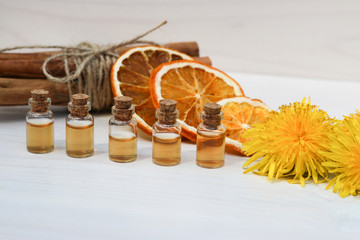 Natural oils in glass jars. Cinnamon. Orange. Flowers of a yellow dandelion. White background, canvas rough fabric and knitted napkin as background. 