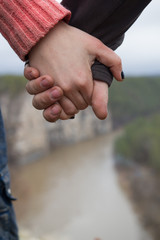 Hands of young couple hikers standing on the edge of a cliff over the mountain river - close up