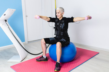 Beautiful senior woman doing exercises in electrical muscular stimulation suit.