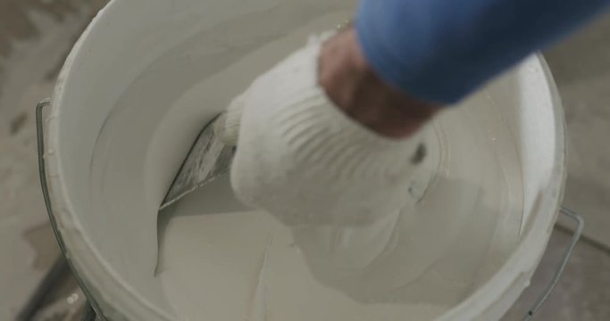 slow motion worker checking putty viscosity in a bucket
