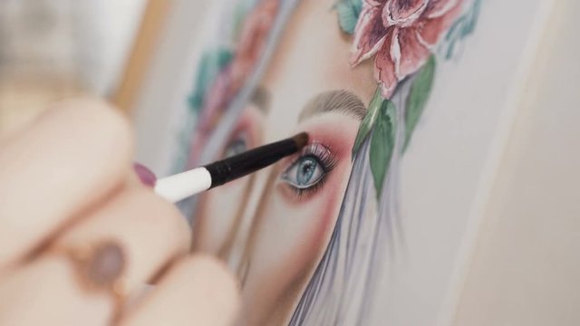 Make-up artist comes up with makeup using a face chart. The artist makeup paints face woman on paper and smears a small brush using palette of eyeshadows for eyes