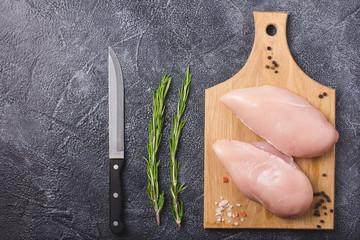 Recipe. Raw chicken breast with spices, rosemary and salt on cutting board. Dark stone background. Flat view. 