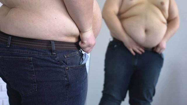 Heavy man tightening jeans belt under fat belly, overeating problem, obesity