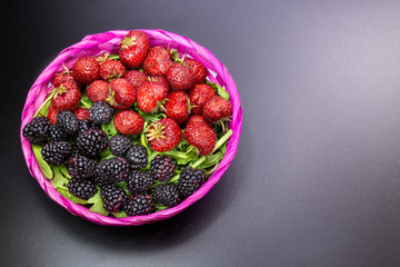 Strawberries and blackberries in a colorful basket on an black table. It is a good and fresh fruit...