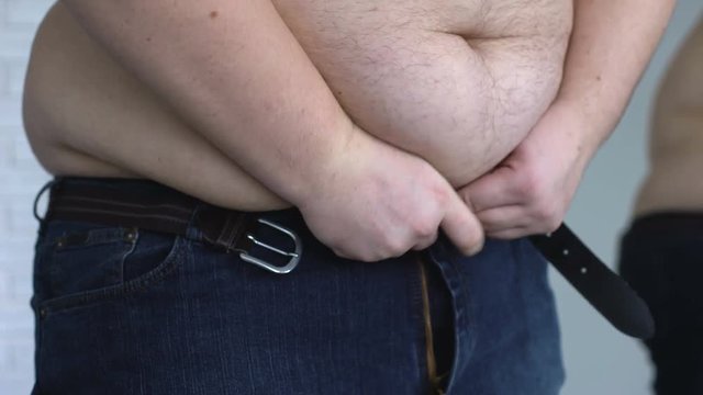 Overweight man zipping up jeans, suffering from stomach fat, hormonal disease