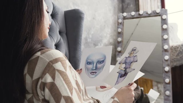 Attractive young fashion designer woman working at art studio. A young woman looks at sketches of design work