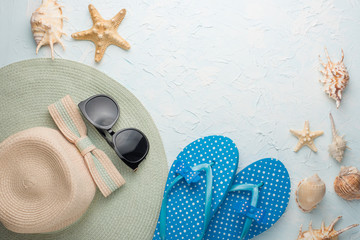 A female hat with round sunglasses and beach slippers. On a blue background, with seashells. With...