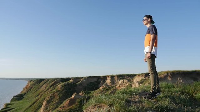 Profile of a vivid man in a baseball cap, sunglasses and a T-shirt standing on the Black Sea coast and observing the sea in summer in slow motion