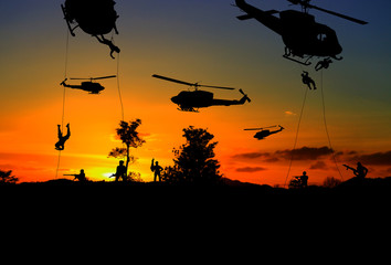 Fototapeta na wymiar Silhouette Soldiers rappel down to attack from helicopter with warrior beware danger On the ground sunset Background blur and copy space add text ( Concept stop hostilities To peace)