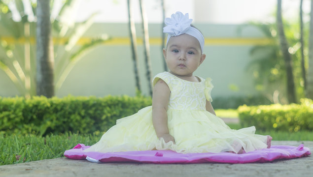 eautiful and white baby, with wreath of flowers, sitting on pink doily on the lawn.  Various expressions and tender emotions.  Yellow dress, brown wicker basket, on spring green grass.