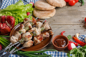 Shish kebab from pork on skewers laid out on a dish. Meat cooked on an open fire. Still life on a wooden background with textiles. Close-up. Place under your text.