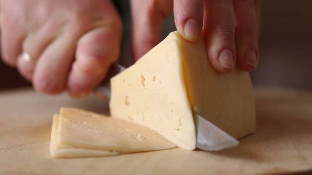 Close-up of female cook or housewife cutting cheese with a knife, slow motion.