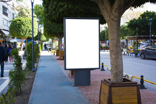 Blank vertical street billboard stand with city background.