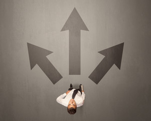 Young contemplating businessman stands in front of brown arrows