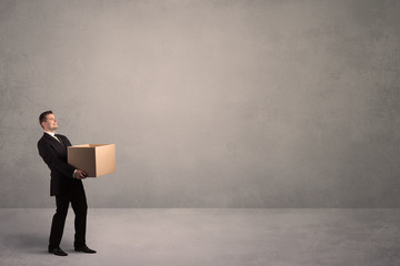 Obraz premium A well dressed young office worker holding an empty paper box with clear concrete wall background concept.