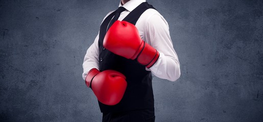 A well dressed sales person standing with red boxing gloves on his hand in front of urban grey wall background concept.