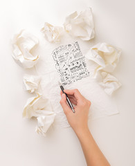 Female hand next to a few crumpled paper balls drawing charts and graphs