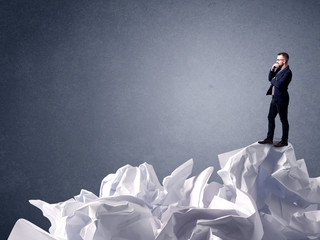 Thoughtful young businessman standing on a pile of crumpled paper 