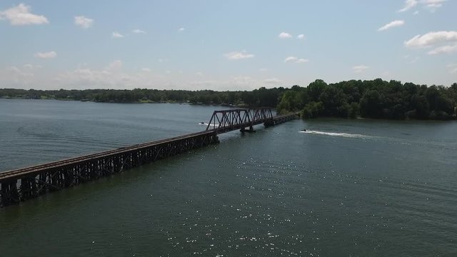 Aerial of Railroad Trestle Over a Lake with Jet ski and Boat Going Underneath
