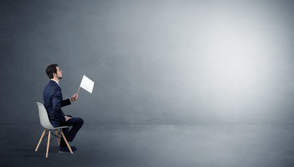 Businessman staying in an empty grey dark room with stuffs on his lap
