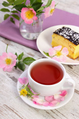 Cup of hot tea with cheesecake and wild rose flower on old board