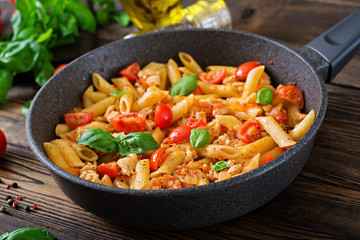 Penne pasta in tomato sauce with chicken, tomatoes, decorated with basil on a wooden table. Italian food. Pasta Bolognese.