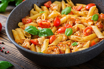 Penne pasta in tomato sauce with chicken, tomatoes, decorated with basil on a wooden table. Italian food. Pasta Bolognese. © timolina