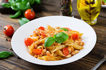 Penne pasta in tomato sauce with chicken, tomatoes, decorated with basil on a wooden table. Italian food. Pasta Bolognese.