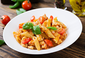 Penne pasta in tomato sauce with chicken, tomatoes, decorated with basil on a wooden table. Italian food. Pasta Bolognese.