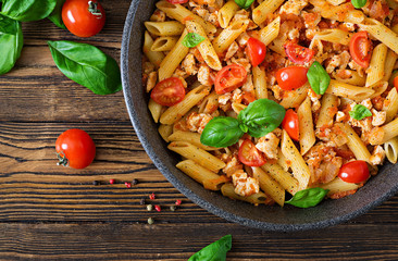 Penne pasta in tomato sauce with chicken, tomatoes, decorated with basil on a wooden table. Italian food. Pasta Bolognese. Top view. Flat lay