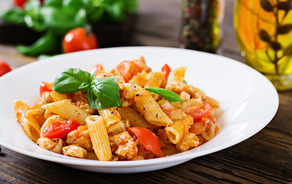 Penne pasta in tomato sauce with chicken, tomatoes, decorated with basil on a wooden table. Italian food. Pasta Bolognese.
