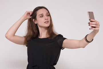 Naklejka premium Portrait of a beautiful brunette girl on a gray background making a selfi with a smartphone