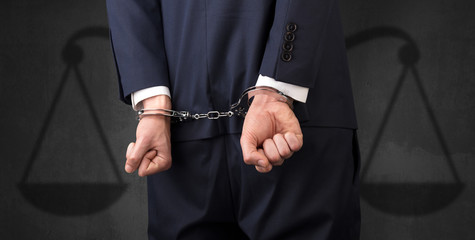 Arrested businessman in handcuffs with hands behind back and justice symbol wallpaper
