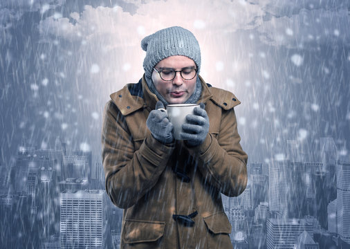 Young man freezing in warm clothing with city concept

