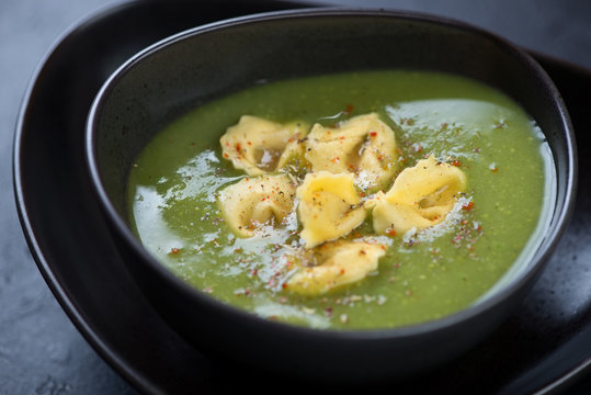 Close-up of broccoli cream-soup with tortellini served in a black bowl, selective focus, studio shot