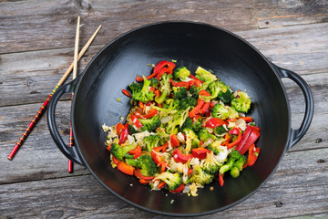 wok with vegetables and chopsticks on wooden ground