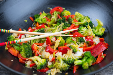wok with vegetables and chopsticks on wooden ground