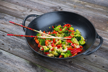 wok with vegetables and chopsticks on wooden ground