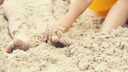 Children's feet are buried in sand. Happy holiday on th e sea coast.