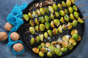 Above view of skewers with roasted brussels sprouts, grated parmesan and walnuts on a metal tray