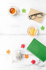 Feminine desk workspace flat lay with diary, eyeglasses, book, tea mug, sweets and felt decor.